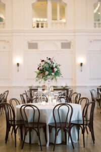 Elegant round table with white cloth, wooden chairs, floral centerpiece, and candles in a bright Louisiana wedding setting.