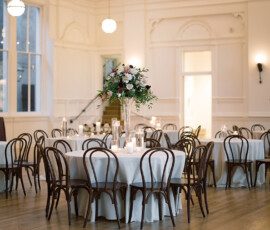 Bright banquet hall with white-clothed round tables, brown chairs, flowers, and candles—ideal for New Orleans weddings.