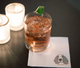 Cocktail with ice and lime on a dog-illustrated napkin, beside two candles—New Orleans wedding inspiration.