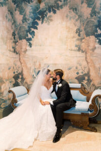 Bride and groom smile on a vintage blue couch at their New Orleans wedding, with a scenic mural backdrop.