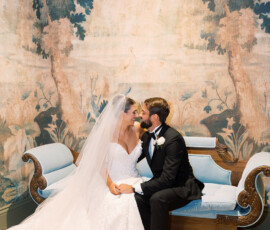 Bride and groom smile on a vintage blue couch at their New Orleans wedding, with a scenic mural backdrop.