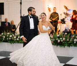 Bride and groom dance joyfully at their wedding with a live band and floral arrangements in the background.