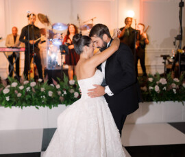 Bride and groom share a romantic first dance on a black and white floor with live band and floral arrangements at the reception.