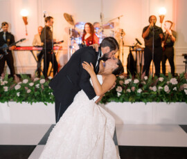 Bride and groom share a romantic dip and kiss on a checkered dance floor with live band and floral decor at their Louisiana wedding.