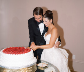 Bride and groom in formal wear smile as they cut their wedding cake at a decorated table, embodying Louisiana wedding joy.