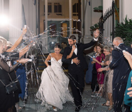 Bride and groom in wedding attire run through guests spraying water or silly string at their joyful New Orleans wedding exit.