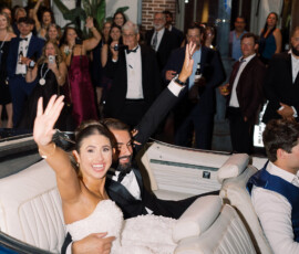 Bride and groom wave from blue convertible, cheered by guests outside CHOPHOUSE after classic Louisiana wedding.