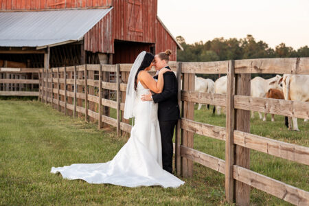 Newlywed brides making a joyful sparkler exit through cheering wedding guests inside a rustic barn venue at the end of the reception.
