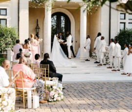Bride and groom wed outdoors before a grand building, with flowers, wedding party, and guests on gold chairs in New Orleans.