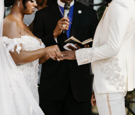 Bride and groom exchange rings at their Louisiana wedding as the officiant stands between them with a microphone and book.