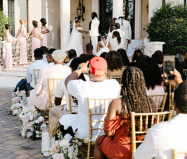 Elegant outdoor New Orleans wedding with gold chairs, pink bridesmaids, floral aisle, and a grand building backdrop.