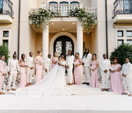 Bride, groom, and wedding party in pink and white pose before an elegant building at a classic New Orleans wedding.