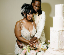 A couple in formal wear cut a white wedding cake together at their elegant reception, pastel flowers on the table.