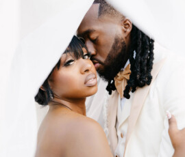 Bride and groom in elegant wedding attire embrace under a sheer veil at their Louisiana wedding; bride faces camera.