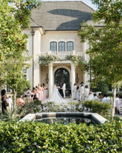 Outdoor wedding ceremony at a grand estate with guests seated beside manicured gardens and a reflecting pool.