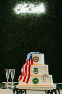 American flag-themed three-tiered cake with military insignias, two champagne flutes, and a glowing “The Smiths” sign.