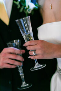 Bride and groom toast with champagne at their Louisiana wedding, she in a white dress and ring, he in a dark suit.
