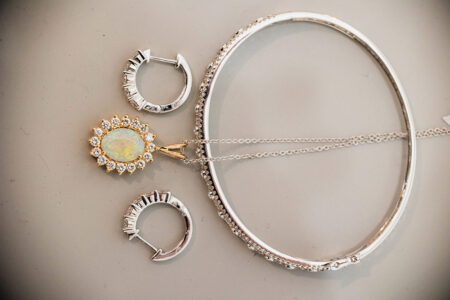 Gold opal necklace, silver bangle, and crystal hoop earrings on a light surface—timeless jewelry for Gulf South weddings.