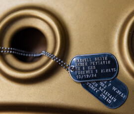 Personalized military-style dog tags engraved with the couple’s names, wedding date, and “Forever & Always” resting against a gold speaker backdrop.