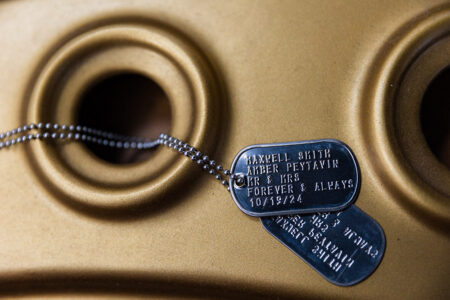 Metallic dog tags on gold surface, engraved with names, date 10/19/24, and “Forever & Always” from a Gulf South wedding.