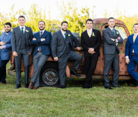 Groom and groomsmen posing in suits beside a vintage rust-colored pickup truck outdoors before the ceremony.