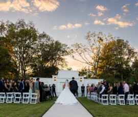 Bride and groom walking down the aisle together at sunset following their outdoor wedding ceremony as guests stand and watch.