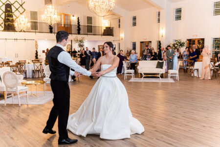 Bride and groom dancing in a bright Louisiana wedding reception hall as guests watch and smile in the background.