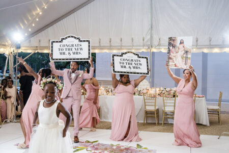 Bridesmaids and groomsmen celebrate on the dance floor holding “Congrats to the New Mr. & Mrs.” signs during the wedding reception.