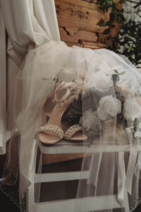 Beige pearl sandals on a white chair with veil, roses, and greenery, perfect for an elegant New Orleans wedding.