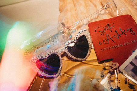 Pearl-rimmed Mrs. Baumgarten sunglasses, Mr. Baumgarten wine glass, and Seth & Ashley napkin at a Louisiana wedding.