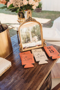 Vintage mirror with “you look like you need a drink,” personalized drink holders, and gold vase—chic New Orleans wedding decor.