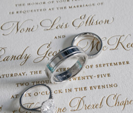 Two silver wedding bands and a diamond ring on a Louisiana wedding invitation with gold ornate initials.