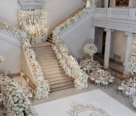 Elegant white Louisiana wedding venue with grand staircase, gold accents, floral décor, round tables, and monogrammed dance floor.