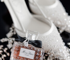 Miss Dior perfume with a black bow in front of crystal-adorned heels and scattered jewelry on a dark surface.