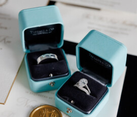 Tiffany & Co. ring boxes with rings rest on wedding invitations and a gold seal, evoking classic Louisiana wedding elegance.