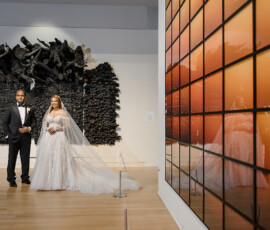 Bride and groom in formalwear by black sculpture, reflected in orange-tiled art, at their New Orleans wedding gallery ceremony.