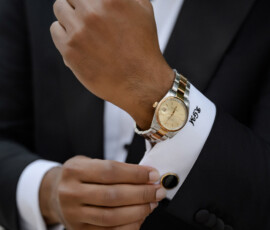 Person in a black tuxedo adjusts cufflink, gold watch and Y&S monogram visible—elegant New Orleans wedding inspiration.