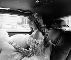 Bride in off-shoulder lace dress sits in luxury car, gazing out window en route to elegant New Orleans wedding.