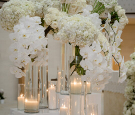 White orchids, roses, and hydrangeas in tall glass vases on pedestals with candles at a Louisiana wedding ceremony.