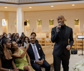 A man in a black suit sings at a stylish Louisiana wedding as smiling guests enjoy the lively, modern celebration.