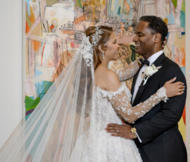 Bride and groom in wedding attire embrace and smile before a colorful abstract painting at their New Orleans wedding.