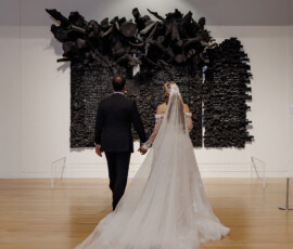 Bride and groom hold hands, walking toward a black abstract wall sculpture after their New Orleans wedding.