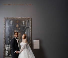 Bride and groom hold hands and smile in front of a painting at the Frederick M. Stafford Gallery, inspiring elegant Louisiana weddings.