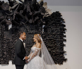 Bride and groom hold hands before a black abstract wall at their elegant Louisiana wedding, in gown and tuxedo.