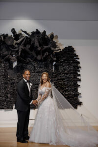 Bride and groom laugh together while posing in front of a dramatic black sculptural art installation inside the museum.
