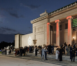 Formally dressed guests gather outside a grand, lit museum at night—an elegant scene evoking a New Orleans wedding.