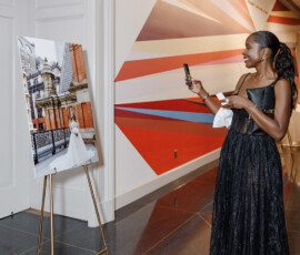 Woman in black dress smiles, photographing a wedding portrait on easel in colorful, modern Louisiana hallway.