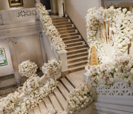 Elegant grand staircase with white and cream flowers, golden monogram, tiered cake—dream New Orleans wedding inspiration.