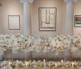 Banquet table with gold chairs, white flowers, and candles in a grand hall—timeless Gulf South wedding inspiration.