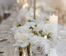 White and blush roses, glassware, a lit candle, and a table number 2 decorate a romantic formal wedding table.